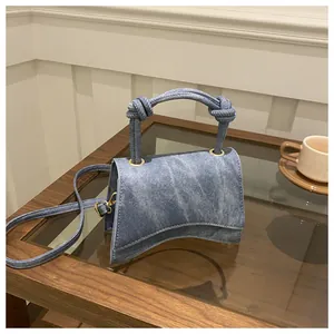 Detailed view of blue denim crossbody bag with curved base and knotted rope handles