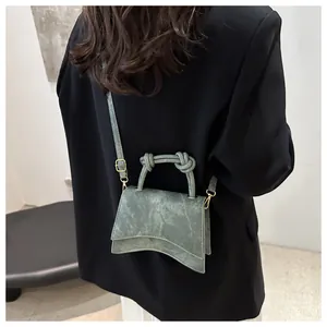 Detail of green suede handbag with unique curved base and knotted handle on black blazer