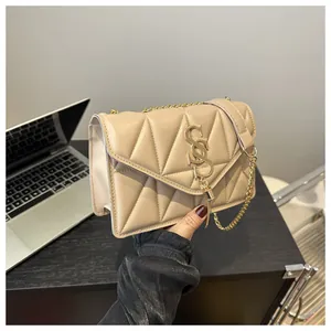 Detail der beigen Stepptasche mit goldenem S-Logo und elegantem Metallkettenriemen