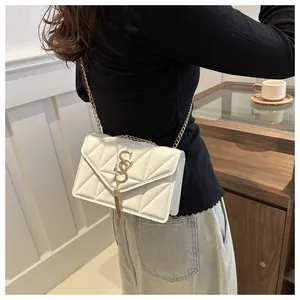 Detail einer weißen Stepptasche mit goldener Kette, Quaste und S-Logo an einem Model