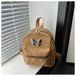 Close-up of caramel pleated mini backpack with a silver metal bow accent and zipper pockets