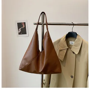 Detail view of large brown faux leather tote bag showing smooth texture on a display rack