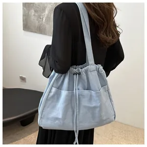 Detail of light blue denim tote bag featuring front pockets and drawstring closure