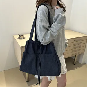 Deep blue denim tote bag with drawstring closure and large front pockets worn on shoulder