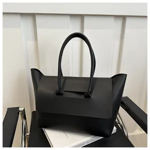 Detailopname van zwarte kunstlederen tote bag met klepsluiting op decoratieve boeken