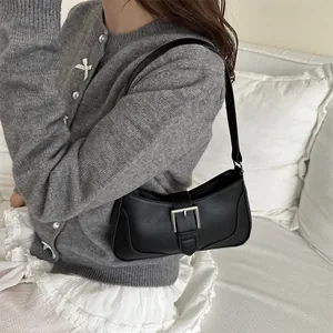 Borsa sottobraccio minimalista in pelle nera con fibbia argentata indossata da una modella