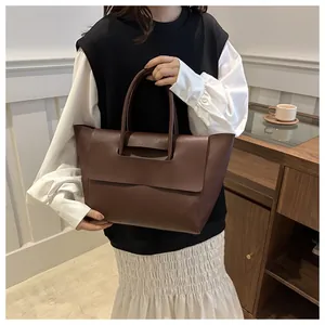 Detailopname van een grote bruine mat leren shopper gedragen door een model in een kamer