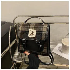 Detailed view of vintage plaid backpack with bear embroidery on metallic stand