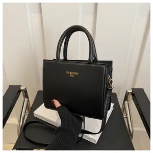 Detail of the black textured square bag featuring gold FASHION BAG text and handle