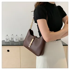 Detail of a brown crescent shoulder bag with golden chain strap on a wooden cabinet