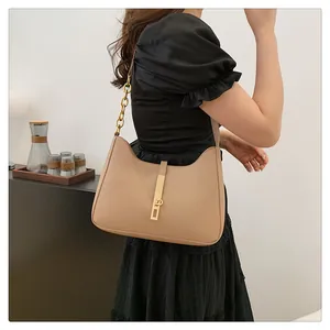 Detail of beige crescent hobo bag featuring gold chain strap and sleek metal lock closure