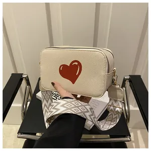 Macro detail of creamy white leather crossbody bag with red heart and woven strap