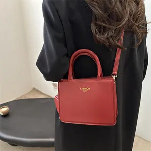 Minimalist red leather square handbag with golden FASHION BAG text worn by model
