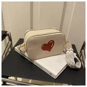 Detail of cream square crossbody bag featuring a red heart and geometric patterned strap