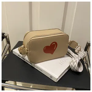 Detail of beige lychee leather camera bag with red heart and geometric pattern strap