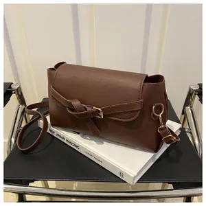 Détail d'un sac bandoulière rétro marron foncé avec boucle nouée sur un livre blanc