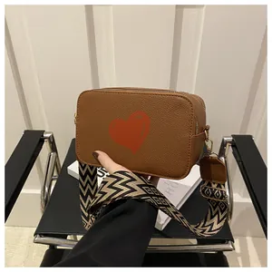 Detail of lychee pattern leather camera bag with red heart and geometric woven strap