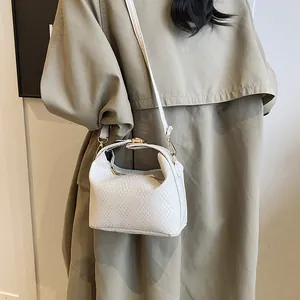 Sac bandoulière blanc à texture tressée et design plié porté sur un trench-coat décontracté