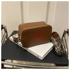 Detail of a brown leather crossbody bag with red heart and patterned wide shoulder strap