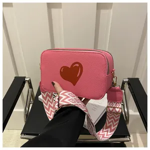 Close-up of pink heart camera bag with textured leather and wide geometric strap