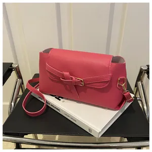 Détail d'un sac bandoulière rose en cuir avec boucle décorative sur un livre blanc