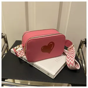 Pink pebbled leather camera bag with red heart detail and woven wide strap
