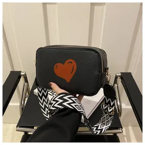 Detail of black pebbled leather crossbody bag with orange heart and woven strap