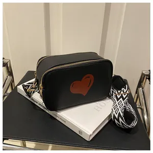 Macro detail of black leather crossbody bag with heart pattern and woven strap