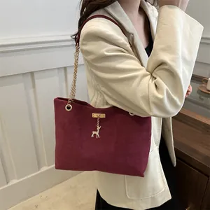 Sac bandoulière bordeaux en daim avec chaîne dorée et pendentif cerf sur modèle