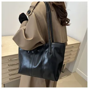 Detail einer großen schwarzen Leder-Tote-Bag kombiniert mit einem khakifarbenen Trenchcoat