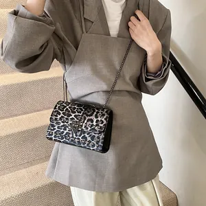 Trendy leopard print crossbody bag with rockstud rivets and gold chain on grey blazer
