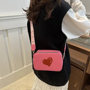 Pink crossbody bag with red heart detail and geometric strap shown on a model