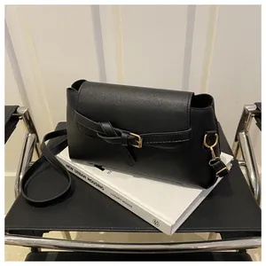 Détail d'un sac à bandoulière en cuir PU noir avec boucle dorée posé sur un livre