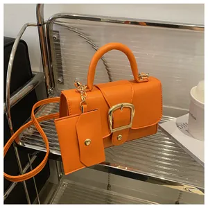 Detail van oranje handtas met litchi-textuur, gouden gesp en een mini-tasaccessoire