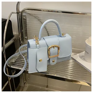 Detail van lichtblauwe crossbodytas met gouden hoefijzergesp en een mini-tasje eraan