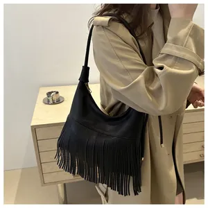 Detail of black lychee texture leather shoulder bag with long tassels on a model