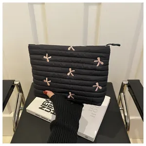 Detail of black quilted pouch with pink bow embroidery held by a gloved hand