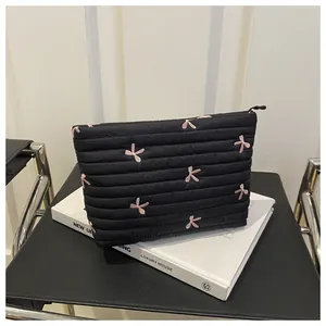Close-up of black quilted makeup bag with pink bow embroidery on a stylish chair
