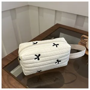 Detail der weißen gesteppten Kosmetiktasche mit schwarzen Schleifen und Tragegurt