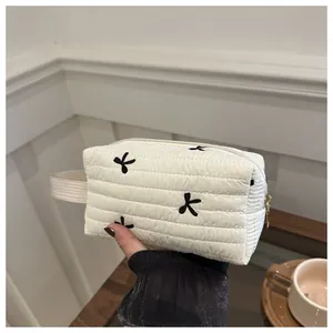 Detail der weißen gesteppten Kosmetiktasche mit schwarzen Schleifen und Goldreißverschluss