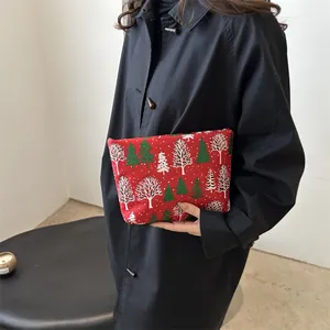 Christmas themed red toiletry bag with festive tree print held against black coat