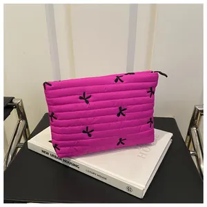 Detail of rose pink quilted cosmetic bag with black embroidered bows on textured fabric