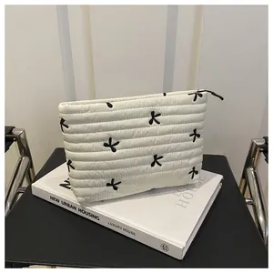 Close-up of quilted cosmetic bag featuring black embroidered bows and metal zipper detail