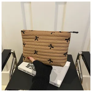 Close-up of khaki quilted makeup bag featuring black bow embroidery and zip detail
