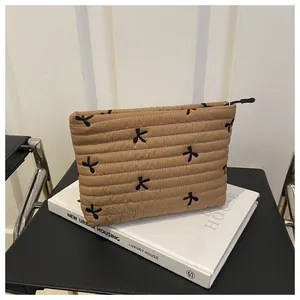 Close-up of khaki quilted toiletry bag featuring black embroidered bowknot patterns