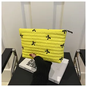 Close-up of bright yellow quilted makeup bag with black bow embroidery and zipper detail