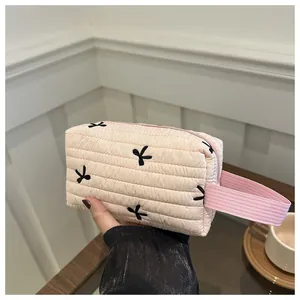 Detail einer rosa gesteppten Kosmetiktasche mit schwarzen Schleifen und Webgriff