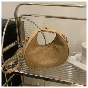 Détail de la texture tressée et du fermoir doré rotatif sur le sac demi-lune beige clair