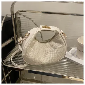 Détail du sac demi-lune blanc tressé avec fermoir doré sur une étagère minimaliste