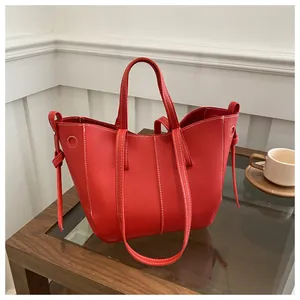 Close-up of a red textured leather tote bag with white contrast stitching and tie details